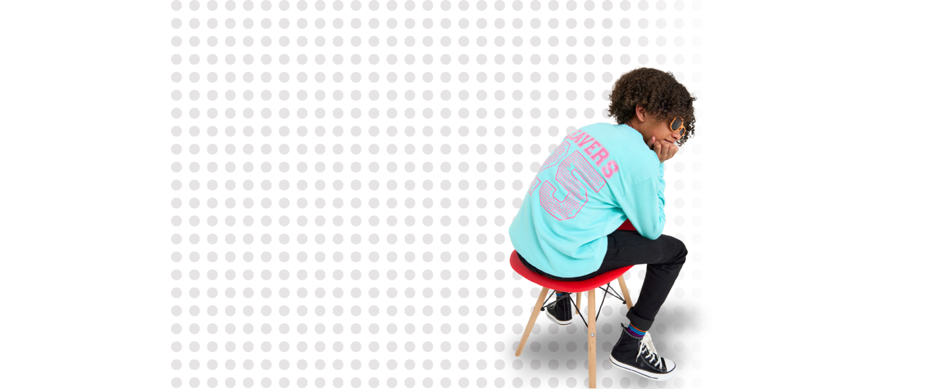 A child models a blue leavers hoodie against a background of grey dots