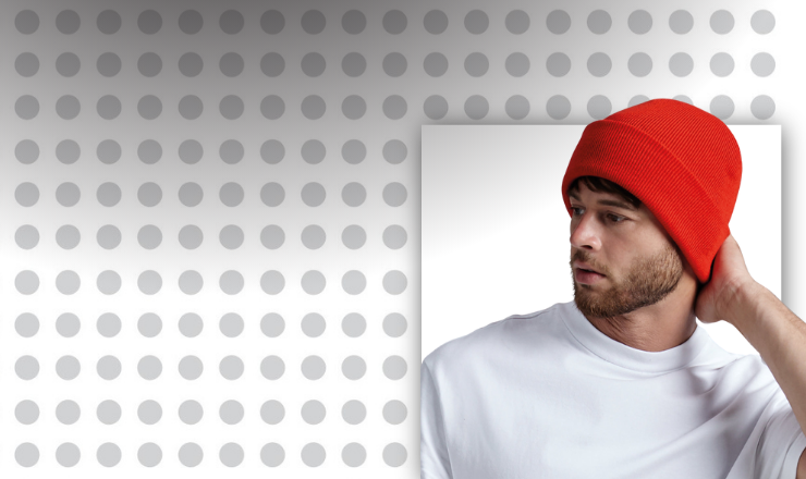 Young adult models a BC045 Beanie in red against a spotted background