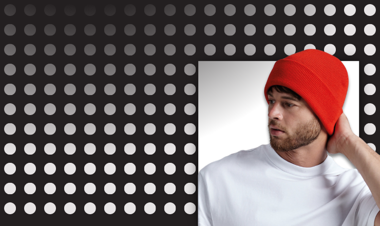 Young adult models a BC045 Beanie in red against a spotted grey background