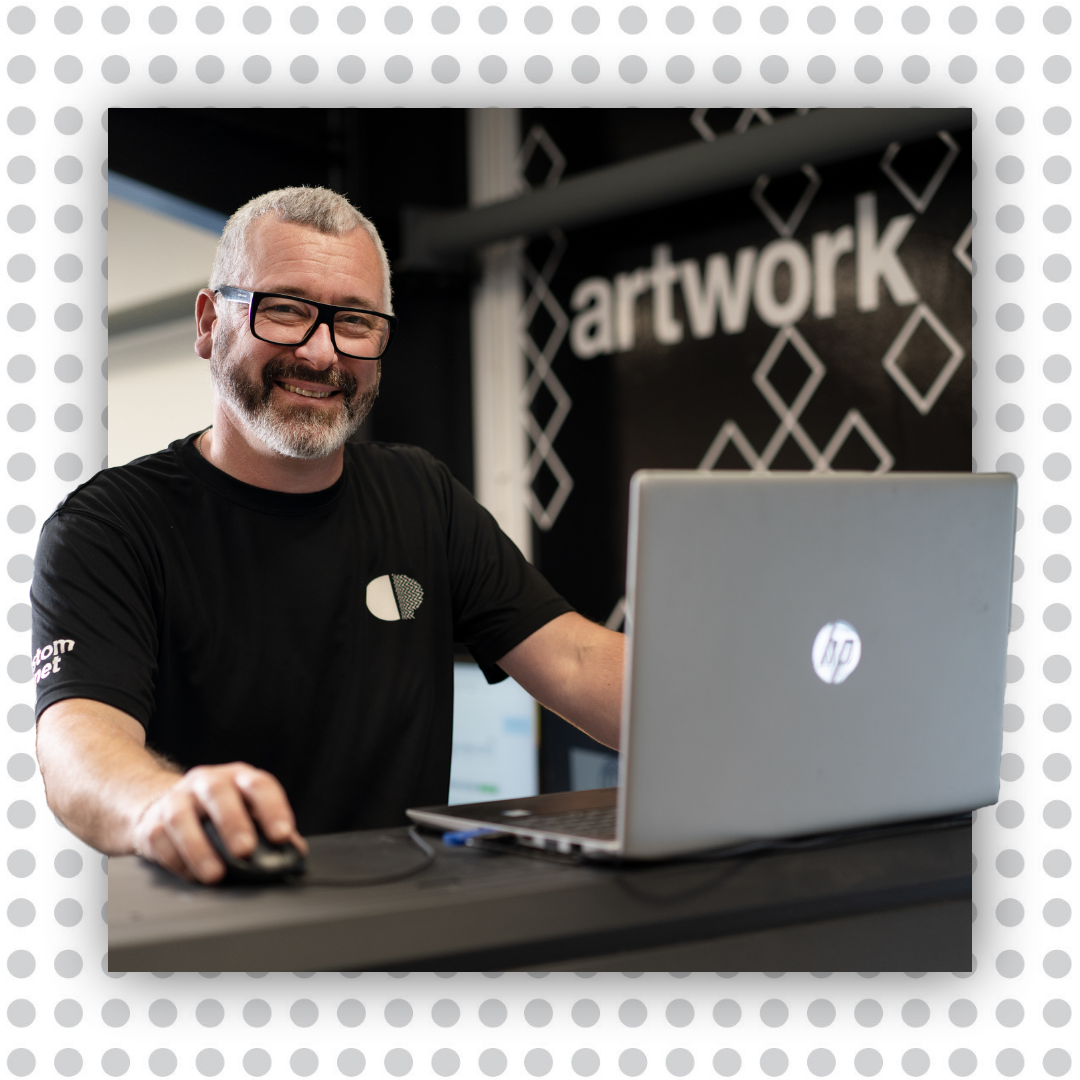 A man sits at a computer, smiling warmly.